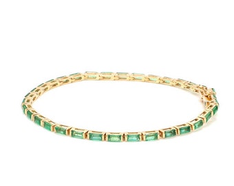 Puede incluir: Un brazalete de oro con una fila de piedras rectangulares de color verde esmeralda.