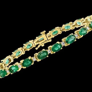 May include: A gold bracelet featuring oval-cut emeralds and small diamond accents. The bracelet has a secure clasp and is set against a black background. The emeralds are a vibrant green color.