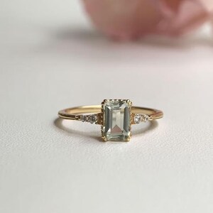 May include: A gold ring with a light green emerald-cut gemstone and small diamonds on the band.