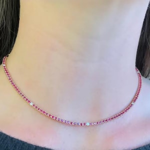 Op de afbeelding: Een delicate ketting met een doorlopende lijn van kleine, heldere rode edelstenen. De ketting wordt om de nek gedragen, waarbij de edelstenen een sprankelend, opvallend effect creëren. Een mooi sieraad.