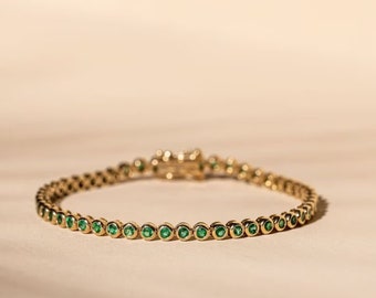 Puede incluir: Un brazalete de oro con una fila de piedras preciosas de color verde esmeralda.