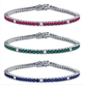 Könnte beinhalten: Drei Tennisarmbänder mit einer silbernen Kette und einer Reihe von Edelsteinen. Das obere Armband hat rote Edelsteine, das mittlere Armband hat grüne Edelsteine und das untere Armband hat blaue Edelsteine.