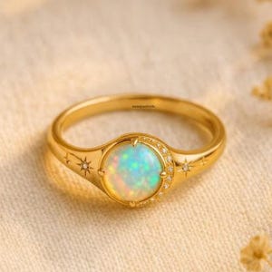 Könnte beinhalten: Ein goldener Ring mit einem großen, schillernden Opal-Mittelstein. Der Ring hat ein Sternenmuster mit kleinen Diamanten und Sternakzenten auf dem Band. Der Opal zeigt Farben wie Blau, Grün und Gelb.