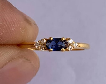 Puede incluir: Un anillo de oro con un zafiro azul ovalado y pequeños diamantes blancos engastados alrededor.