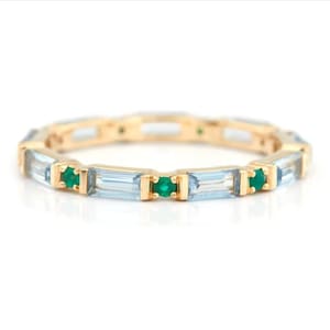 May include: A gold band ring with alternating light blue and green gemstones. The light blue gemstones are rectangular and the green gemstones are round.