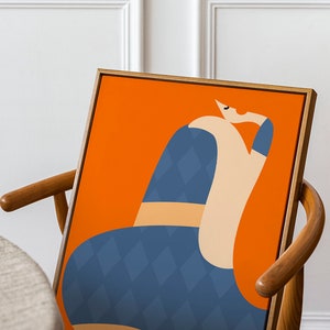 May include: Abstract art print depicting a seated figure. The artwork has a bright orange background with a figure in blue diamond pattern and beige tones. The framed art is displayed on a wooden chair.