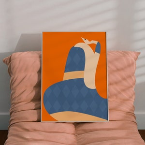 May include: An art print in a silver frame, depicting an abstract figure in a blue diamond-patterned dress against an orange backdrop. The artwork is displayed on a pink cushion, creating a modern aesthetic.