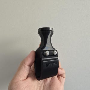 May include: A black, contoured handle component featuring a smooth, glossy top section and a matte, textured lower grip area. Two silver-colored metal bolts are visible on the front, and the text "SNA AERO" is embossed on the lower body.
