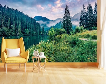 May include: A scenic mountain landscape with a lake in the foreground. The image features a lush green forest with tall pine trees, a misty mountain range in the background, and a calm lake reflecting the sky. The scene is bathed in soft, warm light, creating a peaceful and serene atmosphere.