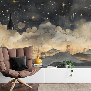 May include: A watercolor painting depicting a city skyline with gold buildings and hills, set against a dark blue night sky with gold stars. The painting is framed by a brown armchair and a white shelf with books and a plant.