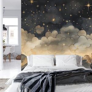 May include: A bedroom with a mural featuring a night sky with gold stars and clouds. The mural is painted on the wall behind a white bed with a gray and white striped blanket.