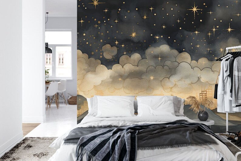 May include: A bedroom with a mural featuring a night sky with gold stars and clouds. The mural is painted on the wall behind a white bed with a gray and white striped blanket.