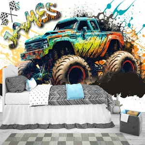 May include: A colorful monster truck with the name "James" painted on the side, against a white background with splashes of paint. The truck is in a bedroom setting with a bed and a storage bin.
