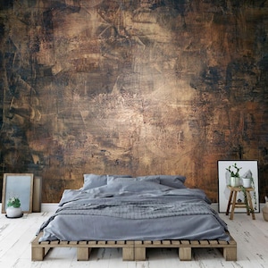 May include: A bedroom featuring a large, textured brown and gold wall mural. A bed with grey bedding rests on a wooden pallet frame. Decorative elements include framed art, a small wooden stool, and a woven basket, all on a white wood floor.