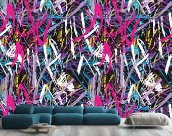 Puede incluir: Papel pintado abstracto de estilo grafiti con una vibrante mezcla de colores. Atrevidos trazos de rosa, blanco, amarillo, azul y morado se superponen sobre un fondo negro. Un moderno sofá seccional azul y una mesa de centro redonda de madera están en primer plano.