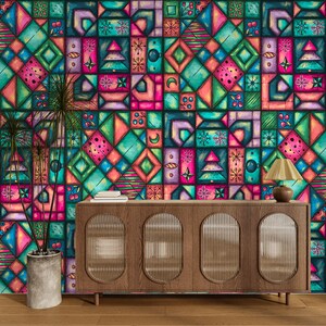 K&ouml;nnte beinhalten: Eine lebendige, farbenfrohe Wandmalerei mit einem geometrischen Muster in T&uuml;rkis, Rosa, Lila und Gr&uuml;n. Das Design zeigt Quadrate und Rechtecke mit verschiedenen Formen und Symbolen. Vor der Wandmalerei stehen ein Holzschrank mit einer Lampe und eine Topfpflanze.