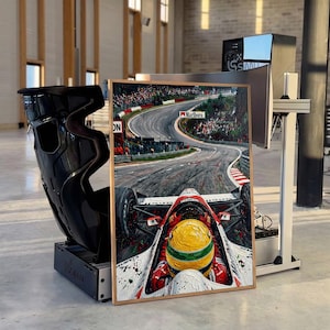 May include: A rectangular framed painting depicting a first-person view from a Formula One race car cockpit. The driver wears a yellow and green helmet. The track shows a curve with spectators and a Marlboro sign. The painting is set next to a black racing seat.
