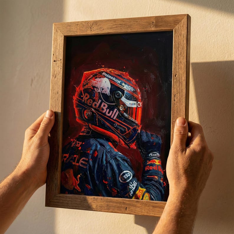 May include: A framed artwork featuring a Red Bull racing driver's helmet and uniform. The artwork is dominated by shades of red and blue, with the Red Bull logo prominently displayed on the helmet. The frame is made of light brown wood.