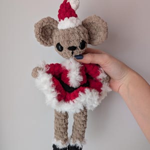 May include: A handmade plush mouse wearing a Santa Claus outfit. The mouse has large, round ears, black eyes, and a small black nose. The Santa outfit is red with white trim, and the hat is red and white. The mouse's legs are tan with black feet.