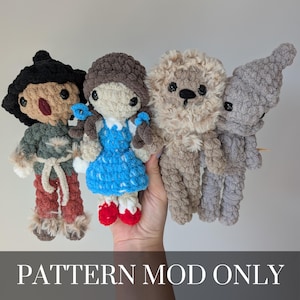 Puede incluir: Cuatro muñecos de ganchillo hechos a mano, incluyendo una niña con vestido azul y zapatos rojos, un león, un espantapájaros y una figura con pelo negro. Los muñecos están hechos con hilo suave y texturizado. El texto "PATTERN MOD ONLY" está en la parte inferior.