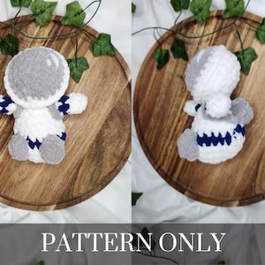 May include: A crocheted plush toy in the shape of a creature with a white body, gray head, and blue and white striped arms. The toy is sitting on a wooden surface.