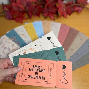 Könnte beinhalten: Ein rosa-grüner Gutschein im Ticket-Stil mit dem Text "HERBST SPAZIERGANG IM SCHLOSSPARK" und dem Wort "Gutschein" auf der rechten Seite. Der Gutschein ist in der Mitte gefaltet und hat ein schwarzes Herz auf der Vorderseite.