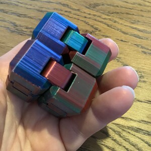 May include: A multi-coloured fidget toy with a blue, red and green colour scheme. The toy is made of plastic and has a geometric design.