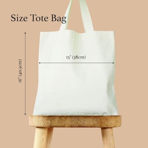May include: A white tote bag with dimensions labeled as 15 inches (38cm) wide and 16 inches (40.5cm) tall. The bag has two handles and is displayed on a wooden stool. The text "Size Tote Bag" is at the top.