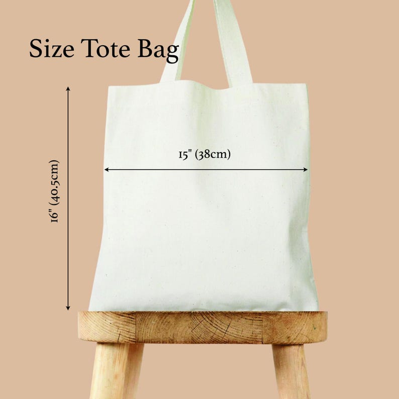 May include: A white tote bag with dimensions labeled as 15 inches (38cm) wide and 16 inches (40.5cm) tall. The bag has two handles and is displayed on a wooden stool. The text "Size Tote Bag" is at the top.