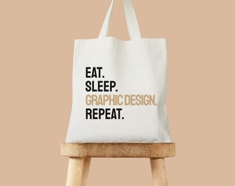 May include: White canvas tote bag with black text that reads "Eat. Sleep. Graphic Design. Repeat."