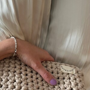 Puede incluir: Un bolso de mano de crochet beige con una etiqueta blanca que dice "AENIC GRAND".