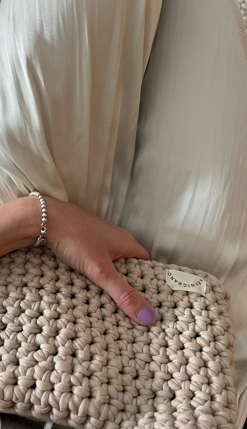 Puede incluir: Un bolso de mano de crochet beige con una etiqueta blanca que dice "AENIC GRAND".