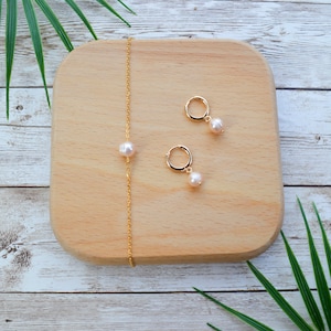 May include: A set of gold pearl jewellery on a wooden surface. The set includes a necklace and a pair of earrings.