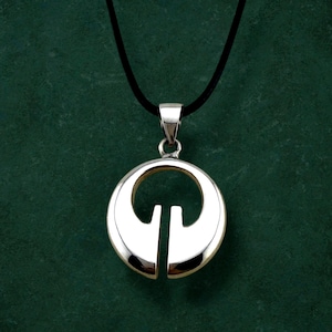 May include: A silver pendant necklace. The pendant has a circular design with a vertical line through the centre. It hangs from a black cord. The pendant has a shiny, reflective surface.