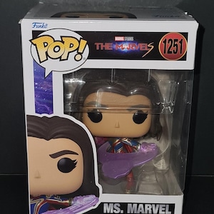May include: A Funko Pop! bobblehead figure of Ms. Marvel from Marvel Studios' The Marvels, in a clear display case. The figure has a purple energy effect and wears a red, blue, and gold costume. The box has the number 1251.