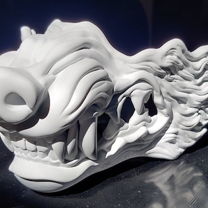May include: A white ceramic sculpture of a snarling wolf's head with a detailed, textured design. The wolf's mouth is open, revealing sharp teeth and a long tongue.