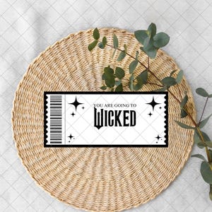 Może przedstawiać: Czarno-biały bilet z napisem "YOU ARE GOING TO WICKED" i gwiazdkami. Bilet leży na tkanej, okrągłej podkładce z gałązką zieleni.