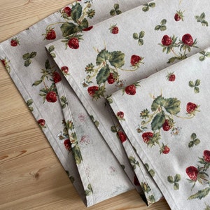 May include: A set of two beige linen table runners with a repeating pattern of red strawberries and green leaves.