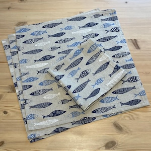 May include: Three linen napkins with a blue and white fish pattern. The napkins are folded and stacked on top of each other.