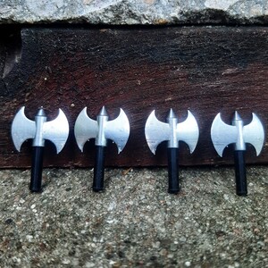 May include: Four silver double-headed axes with black handles. The axes are arranged in a row on a grey concrete surface.