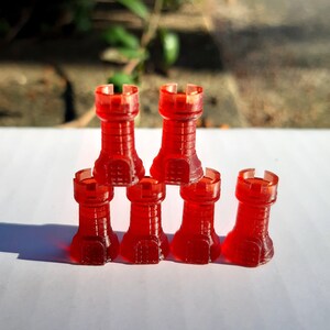 Könnte beinhalten: Sechs rote Plastik-Turm-Schachfiguren, die in Pyramidenform auf einer weißen Oberfläche angeordnet sind.