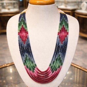 May include: A multi-strand necklace on a mannequin. The necklace has a colour gradient of blue, green, and red beads. The design includes a diamond pattern in the centre, with gold accents at the clasp. A piece of jewellery.