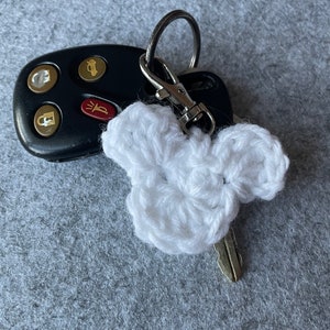 May include: White crocheted heart-shaped keychain attached to a silver key ring and a black car key fob.