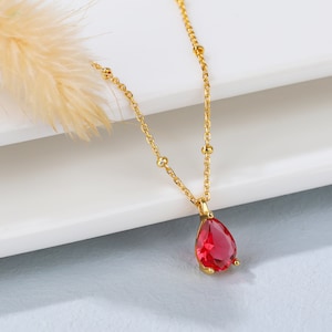 May include: A gold chain necklace with a teardrop-shaped red gemstone pendant.