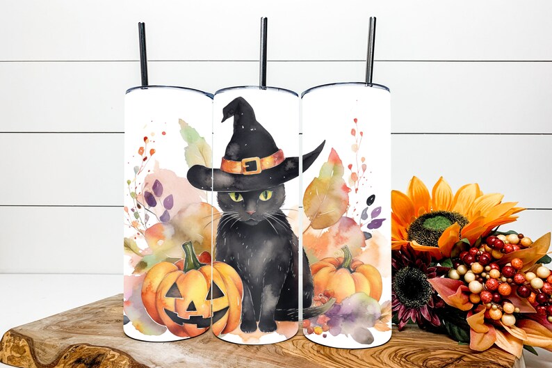May include: Three white Halloween-themed tumblers with black straws. Each tumbler features a watercolor design of a black cat wearing a witch hat, pumpkins, and autumn foliage. The design is in shades of orange, purple, and green.