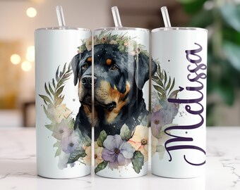 May include: A white tumbler with a Rottweiler dog portrait surrounded by a floral wreath. The dog has black and brown fur and is wearing a flower crown. The name "Melissa" is written in purple script on the side.