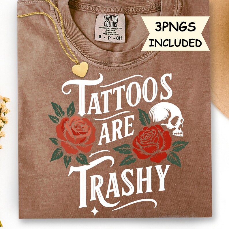 May include: A brown t-shirt with the phrase "Tattoos Are Trashy" in white, featuring red roses and a skull graphic. The shirt includes a gold heart pendant necklace. The tag reads "Comfort Colors".