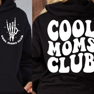 May include: Black hoodie with a white graphic on the front of a skeleton hand making a rock and roll sign with the text "Cool Moms Club" and the same text in white on the back in a retro font.