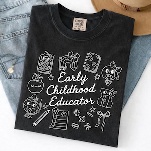 May include: Black t-shirt with white graphic illustrations and the text "Early Childhood Educator." The design includes a calculator, rainbow, notebook, lightbulb, apple, globe, pencil, and other school-themed elements. The shirt is a Comfort Colors brand.