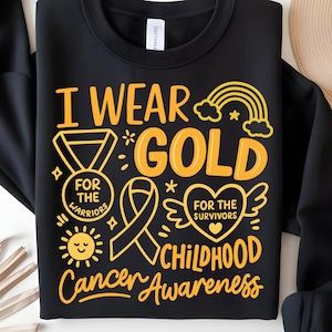 May include: Black sweatshirt with the text "I Wear Gold" in yellow, along with a ribbon, rainbow, and sun graphic. The text also includes "For the Warriors" and "Childhood Cancer Awareness."